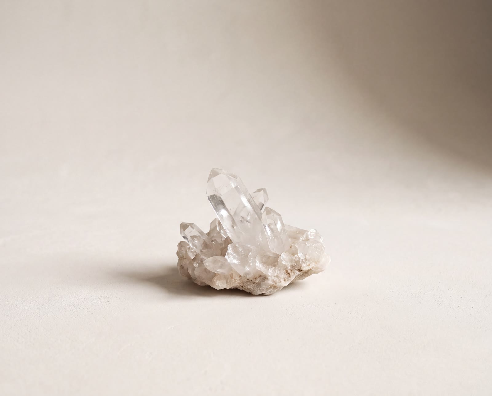 A raw clear quartz cluster standing in soft window light on a warm limestone ground